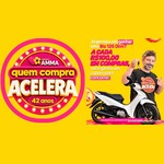 Arte da promoção Grupo AMMA Quem Compra Acelera 42 anos: selo rosa e amarelo à esquerda e, à direita, homem sorridente segurando chaves ao lado de uma moto Honda Biz branca, com o texto "A cada R$100,00 em compras, você ganha um cupom para concorrer".
