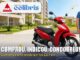 Motocicleta Honda Biz 125 ES vermelha estacionada em condomínio residencial ao lado de uma família sorridente, com logos da DMC Construtora e do Reserva dos Colibris e o texto Comprou. Indicou. Concorreu!