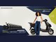 Mulher de cabelos cacheados, regata branca e calça jeans, apoiada em uma moto elétrica preta ao lado do texto "Você de jeans e moto nova", com os logotipos Sawary Jeans e Caedu e uma fila de dez motos no canto inferior esquerdo.