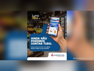 Mão segurando um celular com o aplicativo SuperLuna aberto ao lado do texto "Ainda não podemos contar tudo. Mas podemos dar uma dica: baixe o app no seu celular", em um corredor de hortifruti, com as marcas Luna Mais+ e SuperLuna Supermercados.