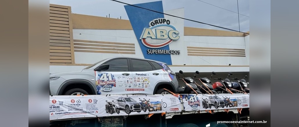 Show de Prêmios ZABCÊ 41 Anos Carreta de aniversário do ZABCÊ Supermercados com um Chevrolet Tracker prata e motos sobre a plataforma, em frente à fachada do Grupo ABC, com faixa do Show de Prêmios 41 Anos