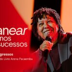 Djavan sorri e canta ao microfone em um palco iluminado em tons de vermelho e laranja, ao lado do logo Djavanear 50 anos só sucessos, do selo UOL 30 anos e do texto 35 pares de ingressos, 12/12/2026, Mercado Livre Arena Pacaembu.