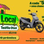 Arte da promoção Rota Local Teófilo Otoni, um movimento Stone, com moto Honda Biz cinza, TV, notebook, smartphone e cartão presente sobre fundo amarelo e laranja, com a frase "A cada R$50,00 = uma chance de ganhar".